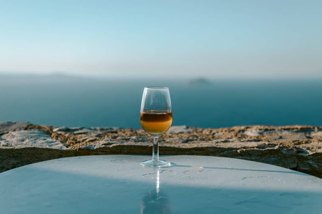 Glass of wine on an outdoor table overlooking the blue Aegean Sea at a winery in Serifos, Greece.