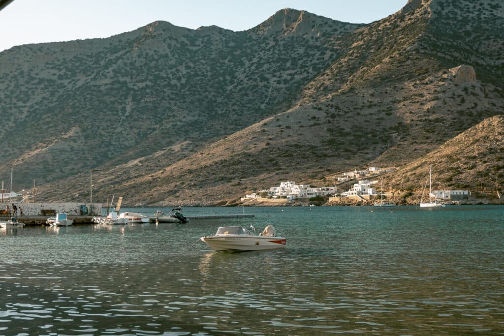Boats floating in Kamares harbor with whitewashed buildings along the shoreline and rugged mountains rising behind them in Sifnos.