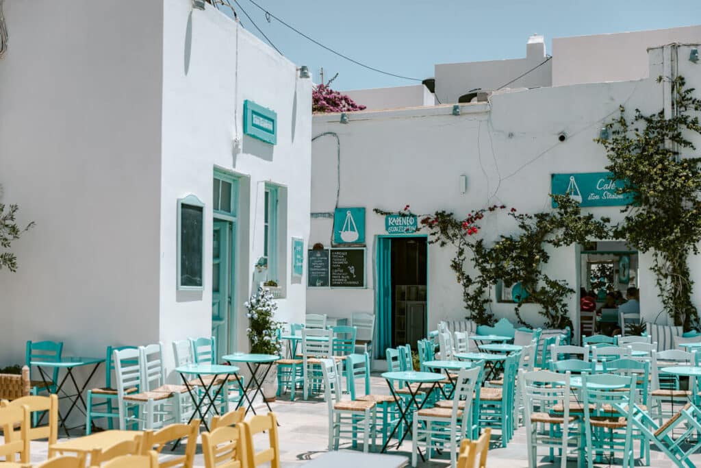 Outdoor café with turquoise, white, and yellow chairs surrounded by whitewashed buildings and flowering vines in Chora, Serifos.