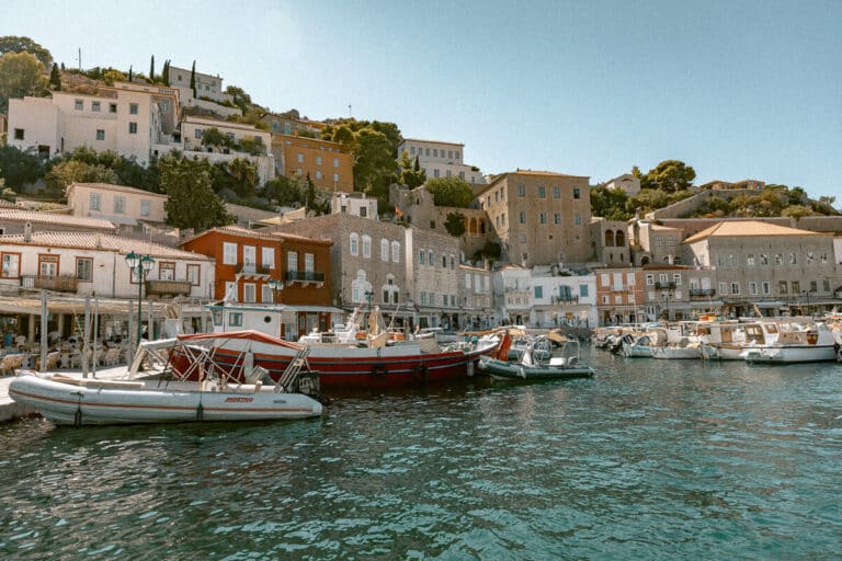 Hydra or Spetses comparison featuring Hydra’s waterfront harbor with traditional stone mansions, colorful buildings, and boats along the turquoise water.