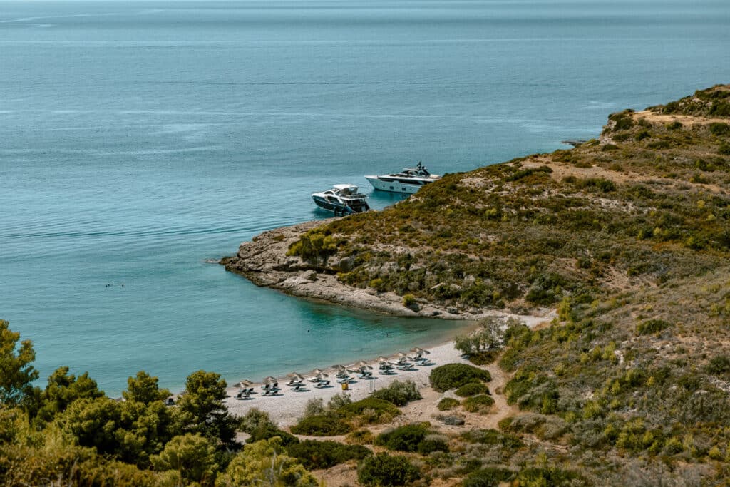 Xilokeriza Beach in Spetses tucked into a rocky cove with turquoise water, rows of sunbeds and umbrellas, and boats anchored offshore.