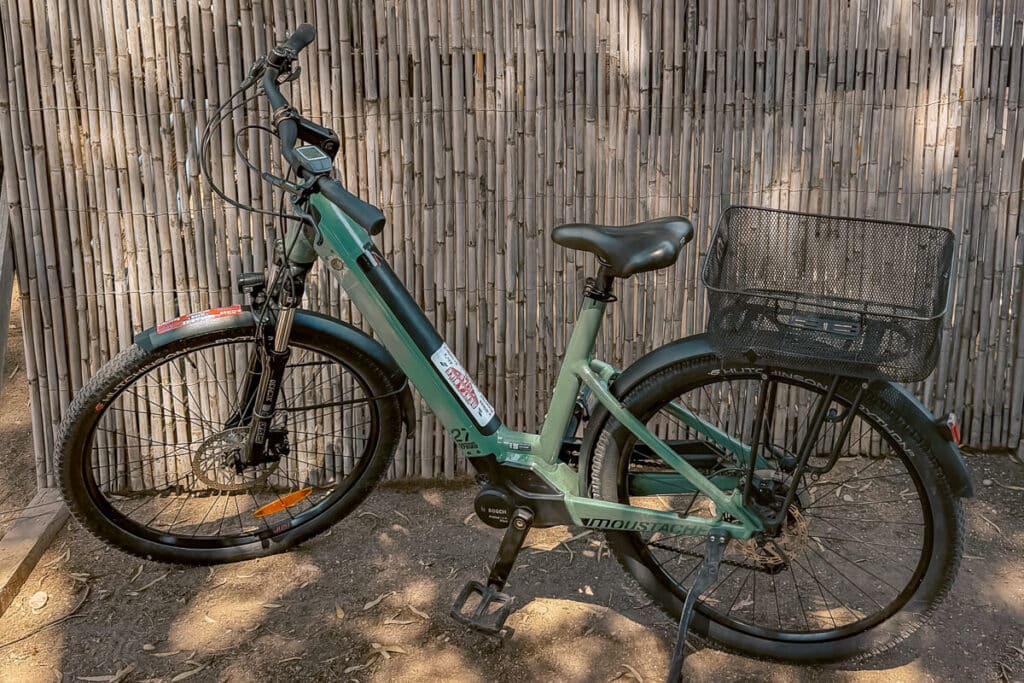 Green e-bike with a rear basket parked beside a bamboo fence while exploring Spetses, Greece.