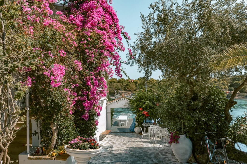 Bright pink bougainvillea surrounding a stone patio with outdoor seating and views of the sea in Spetses, Greece.