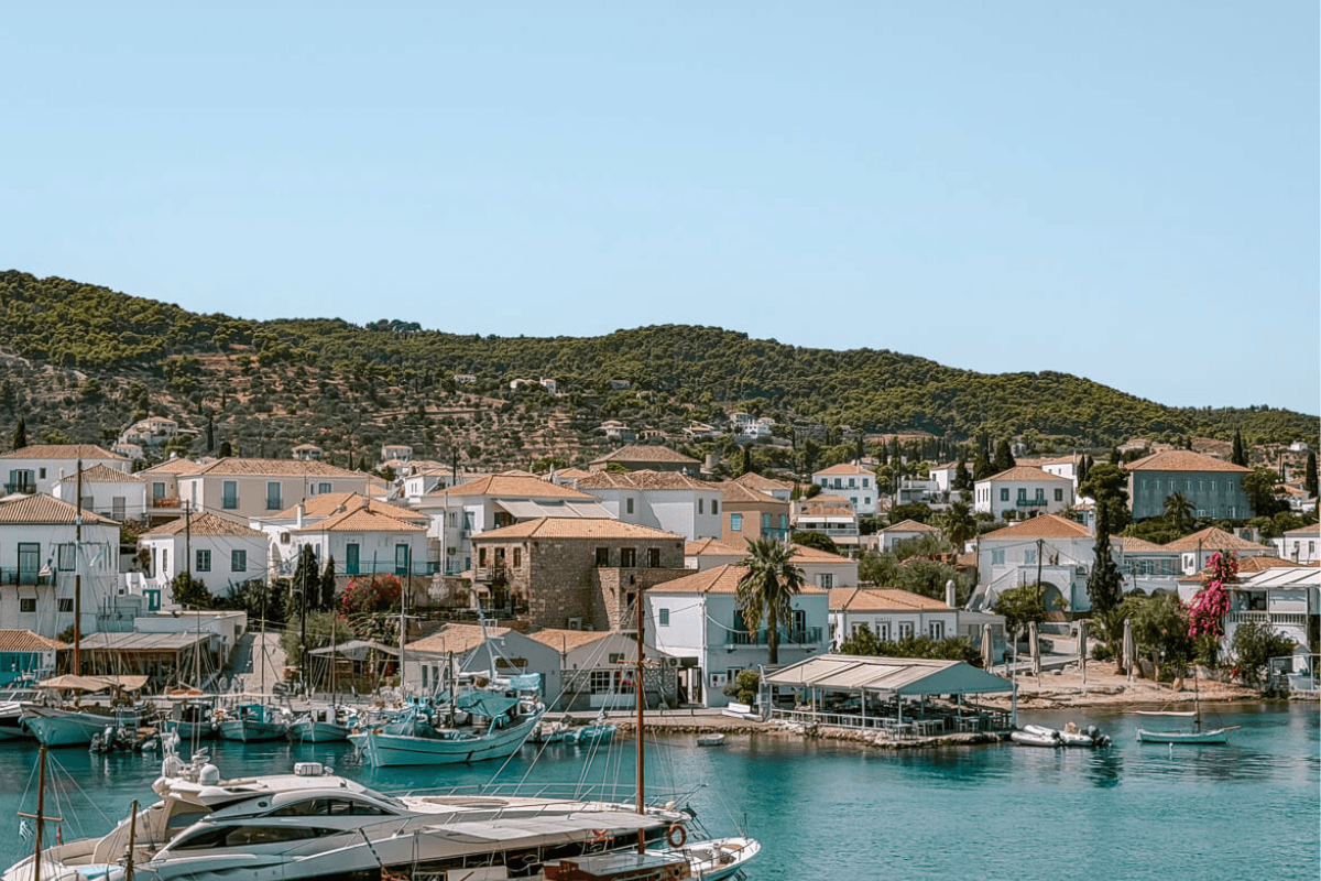 Things to do in Spetses, Greece, with boats in the turquoise harbor surrounded by traditional white houses with terracotta roofs and green hills.