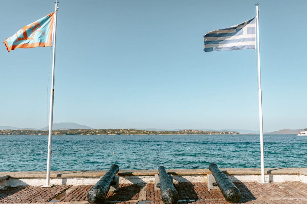 Greek flag flying above historic cannons on the waterfront overlooking the sea in Spetses, Greece.