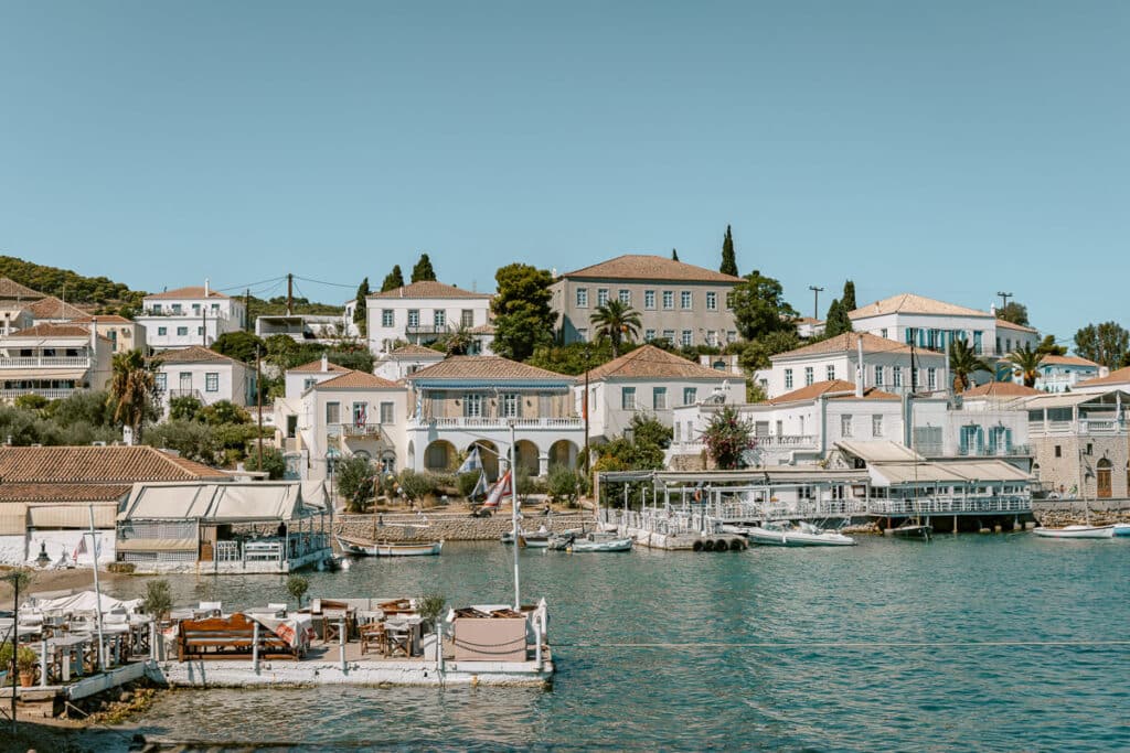 White traditional houses with tiled roofs overlooking boats and turquoise water in the Old Harbor of Spetses, Greece.